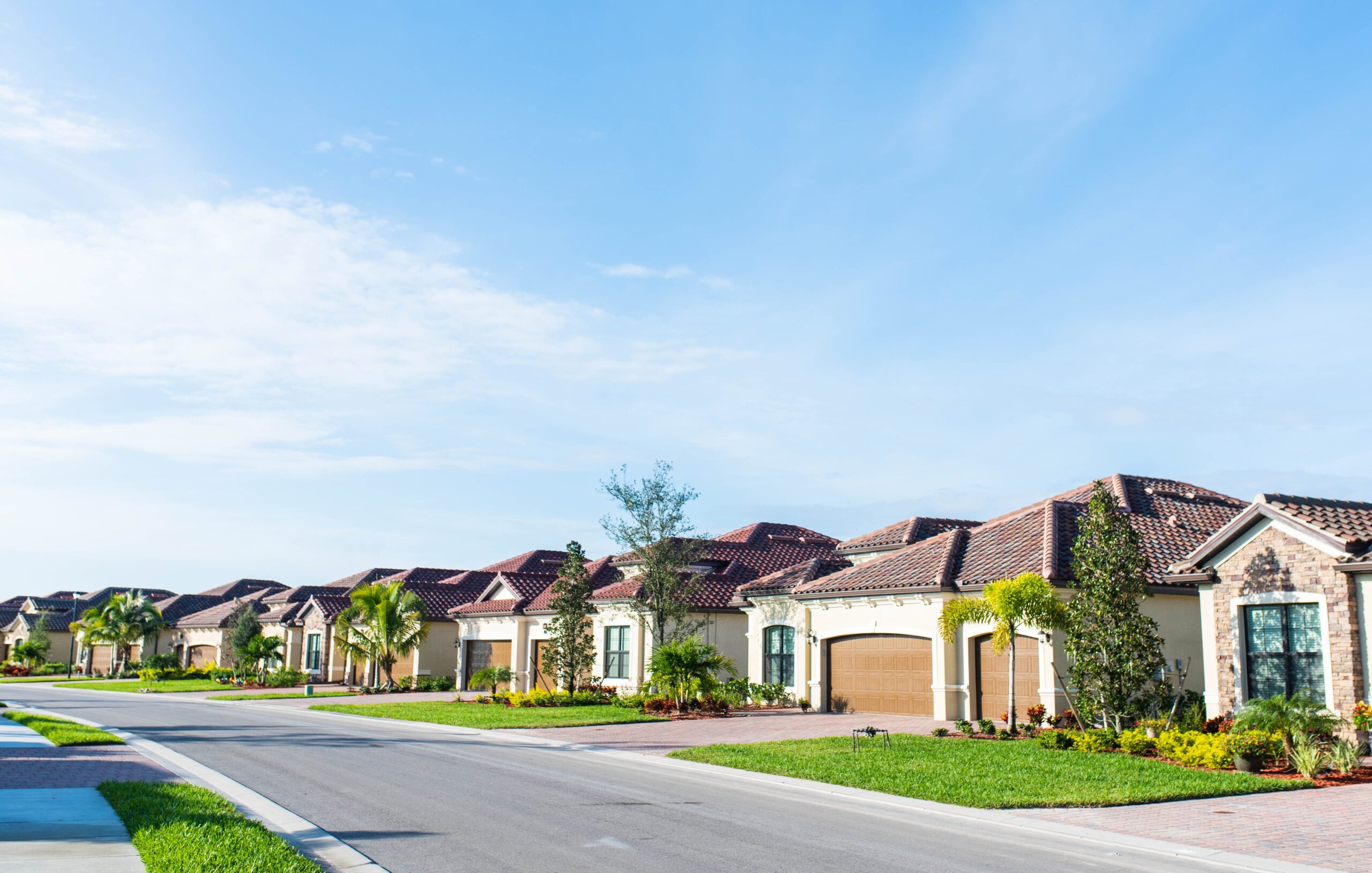 A suburban neighborhood featuring homes with freshly mowed lawns. Clear blue skies, and the sun is shining.