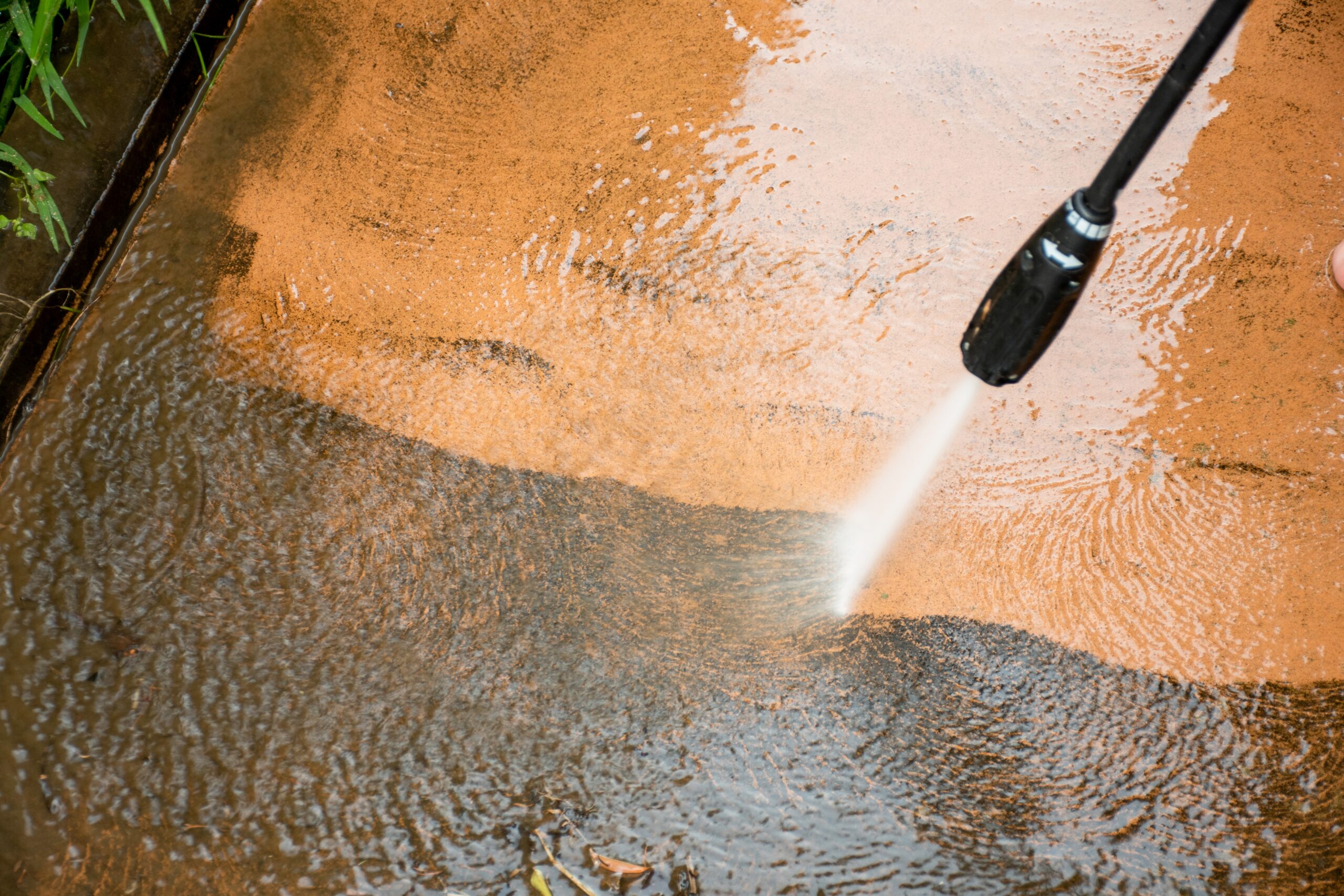 A pressure washer hose cleaning dirt off of the walkway.